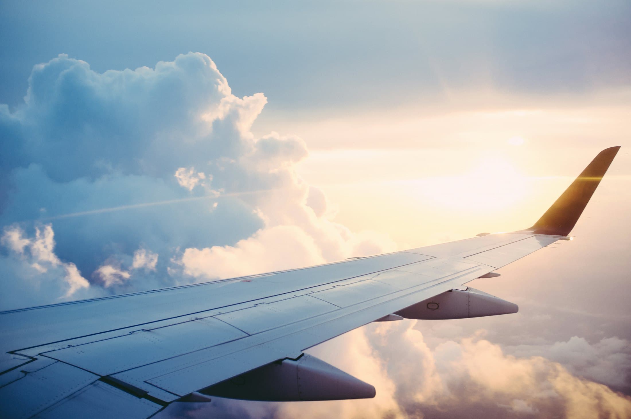 An aircraft wing above golden clouds in a bright sky