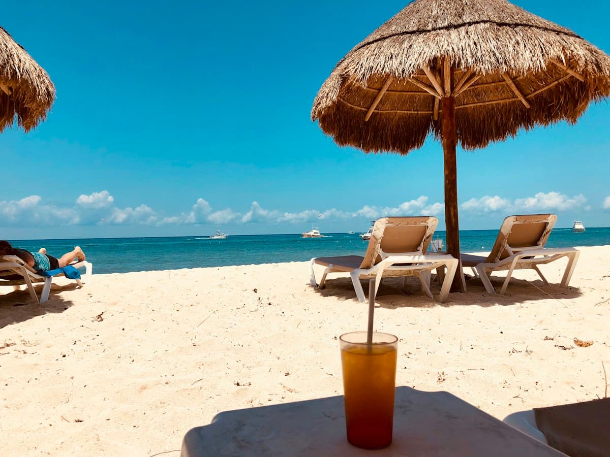 Beach loungers under a thatched parasol by the sea