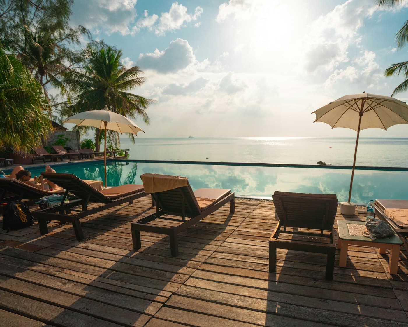 Wooden sun loungers and parasols on a deck above an infinity pool and the sea